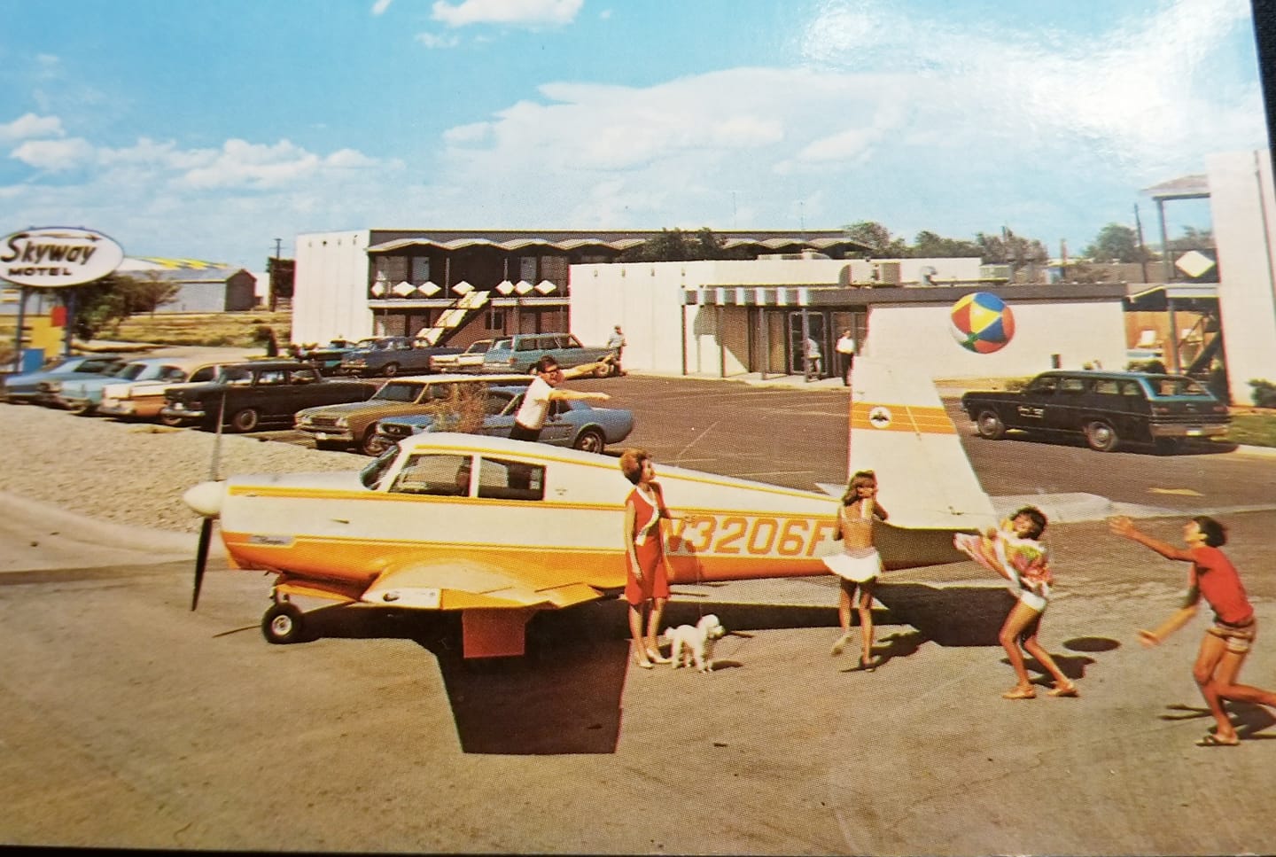 Vintage postcard advertising the Skyway Motel, showing a single-engine aircraft parked outside the motel among 1960s cars